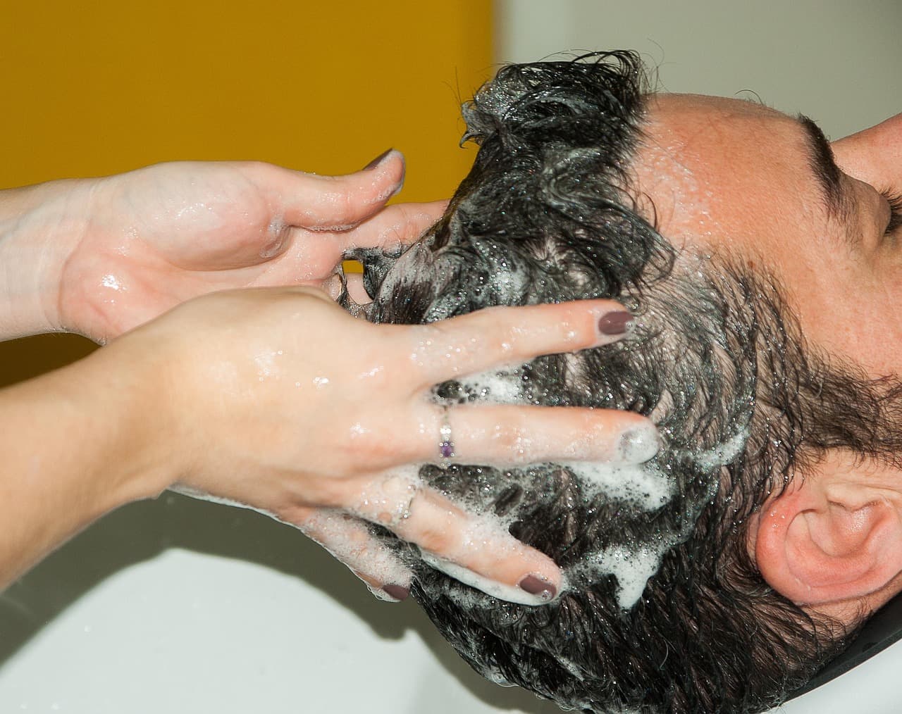 Hands massaging shampoo into dark hair at the basin
