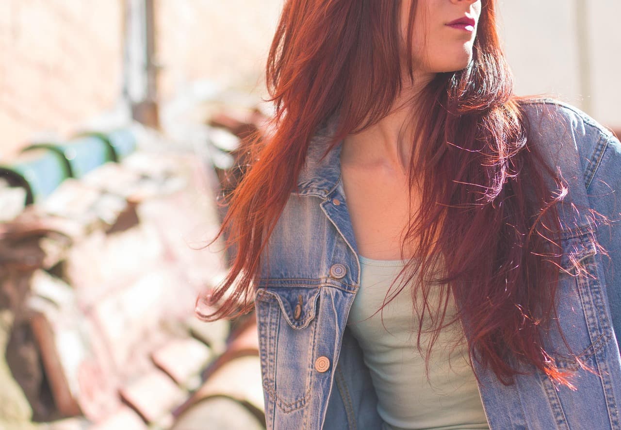 Long, deep auburn-red hair falling over a denim jacket