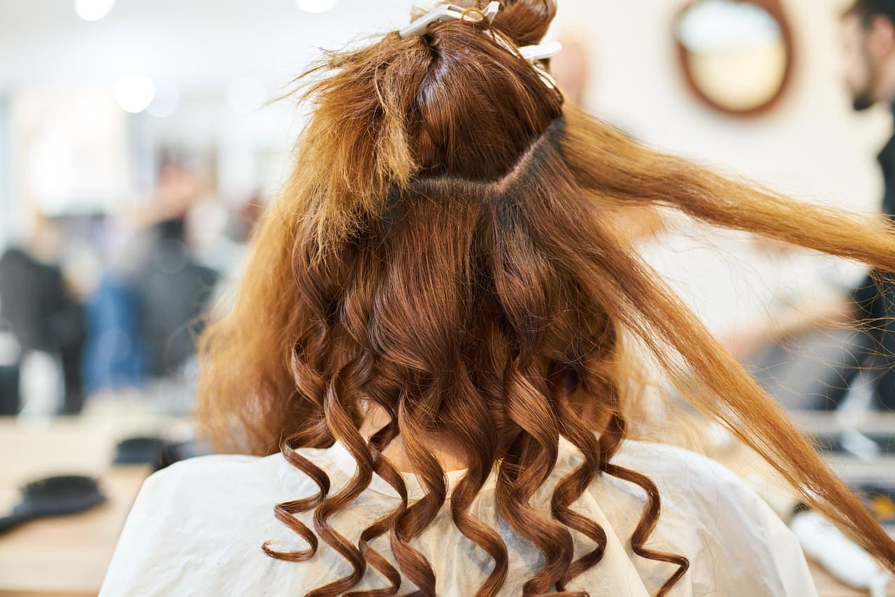 A stylist sectioning long copper curls at the back of the head