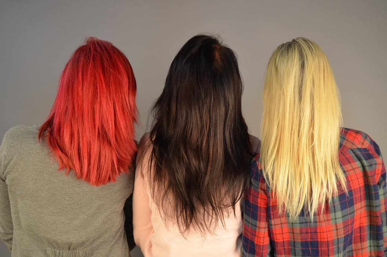 Three women from behind: bright red, dark brown and golden blonde hair